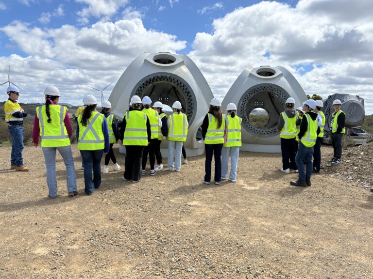 Group of high school students wearing hi-vis inspecting wind turbine component